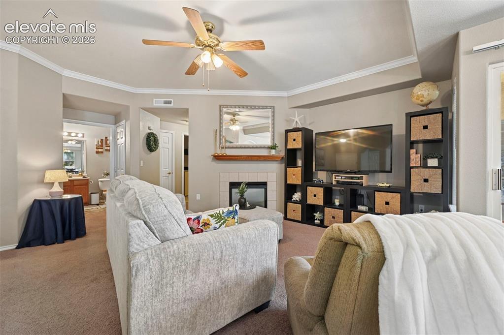 3715 Riviera Grove, Unit 101 Colorado Springs, CO 80922 - Photo 22 of 36 Living area featuring a fireplace with a tile surround and wood mantel, crown molding, and a ceiling fan