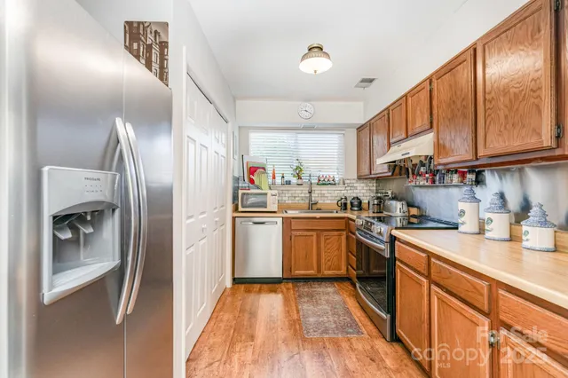 a kitchen with stainless steel appliances granite countertop a refrigerator a sink dishwasher a oven with wooden cabinets and floor