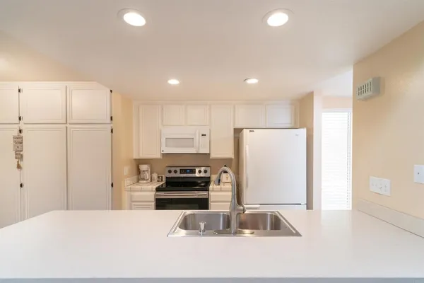 a kitchen with kitchen island granite countertop a refrigerator a stove a sink and white countertops with wooden floor