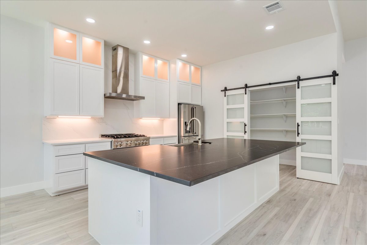 1215 Howard Street Taylor, TX 76574 - Photo 2 of 37 Kitchen featuring range exhaust hood, pantry with barn door, light wood finished floors, high end fridge, and white cabinets