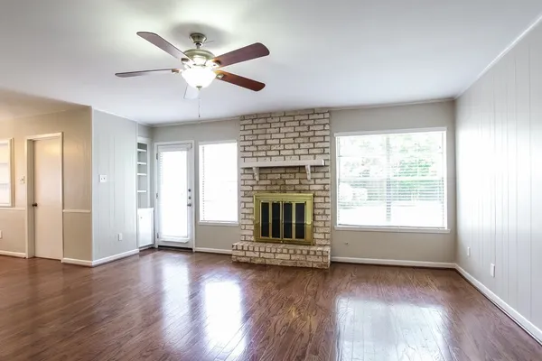 an empty room with wooden floor fan and windows
