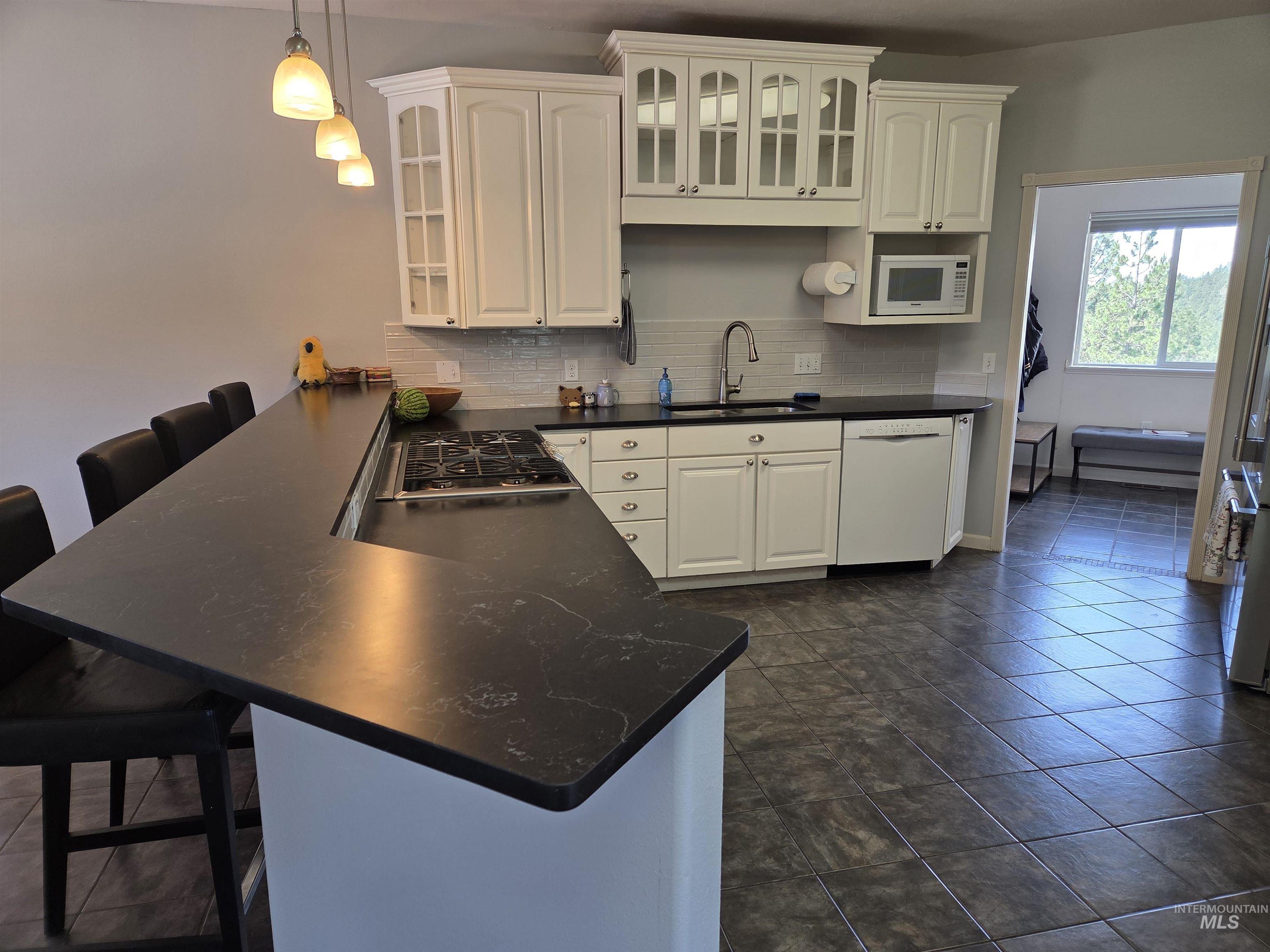 1085 Wallen Road Moscow, ID 83843 - Photo 10 of 50 Kitchen featuring a large dark-toned countertop island with pendant lighting, white cabinetry, a built-in gas range, a white dishwasher, and dark-toned tile flooring