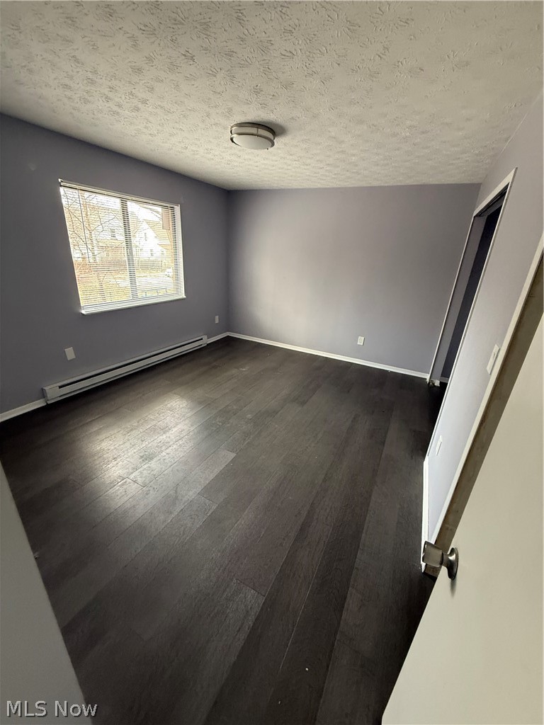 662 Sumner Street Akron, OH 44311 - Photo 5 of 10 Unfurnished room featuring a baseboard heating unit, dark wood-style floors, and a textured ceiling