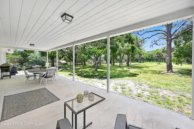 a view of a patio with table and chairs potted plants and floor to ceiling window