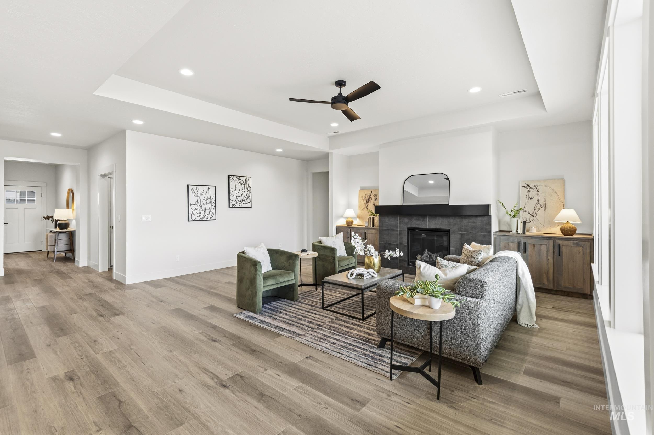 1988 West Bittern Street Nampa, ID 83686 - Photo 15 of 34 Living area with a raised ceiling, a glass covered fireplace, a ceiling fan, light wood-style flooring, and recessed lighting