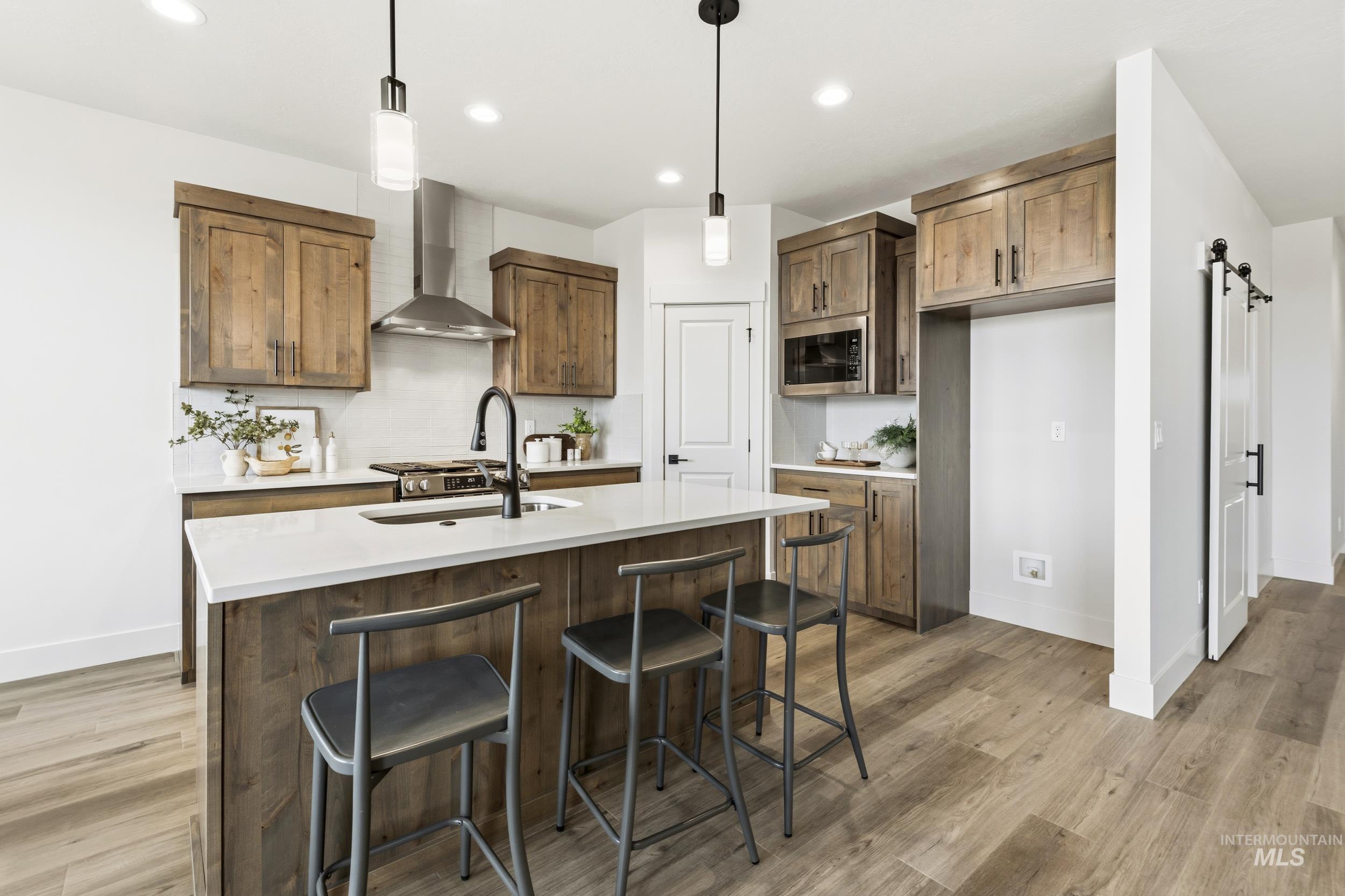 1988 West Bittern Street Nampa, ID 83686 - Photo 18 of 34 Kitchen with hanging light fixtures, a breakfast bar area, a center island with sink, light wood-style floors, and a barn door