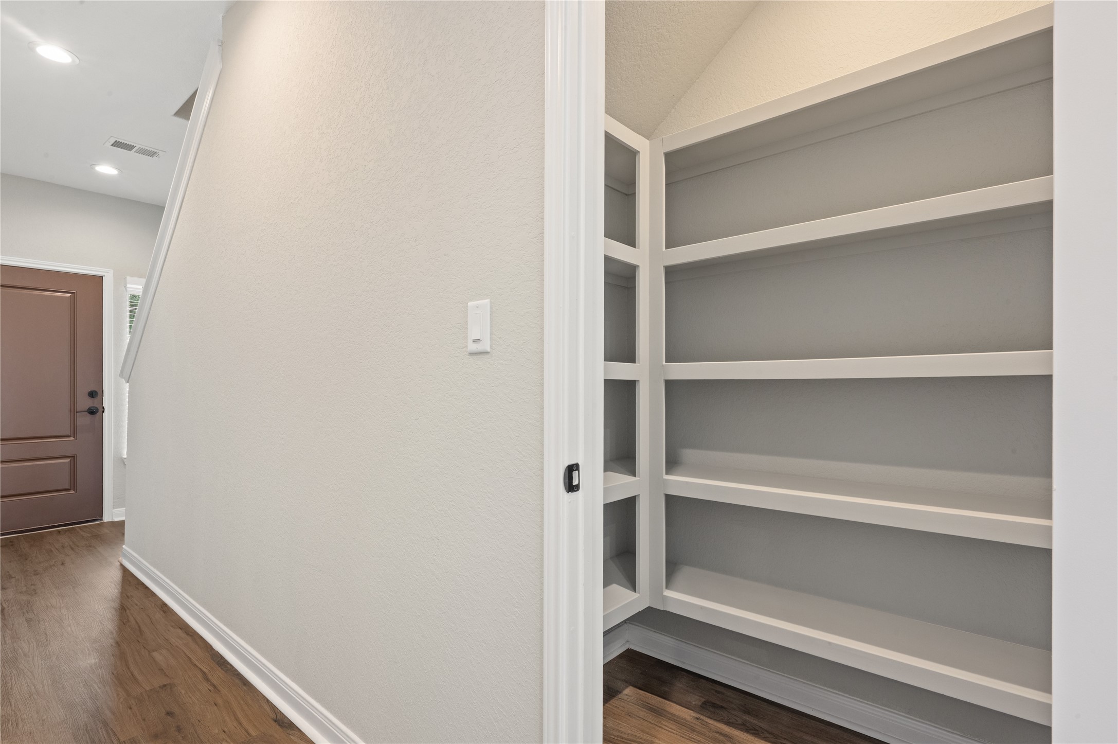14010 Longstreet Road, Unit 2 Willis, TX 77318 - Photo 22 of 29 This photo features a hallway with wood flooring leading to a front door. To the right, there is a spacious, built-in shelving unit under the stairs, ideal for storage or display. The area is well-lit and has a modern, clean design.