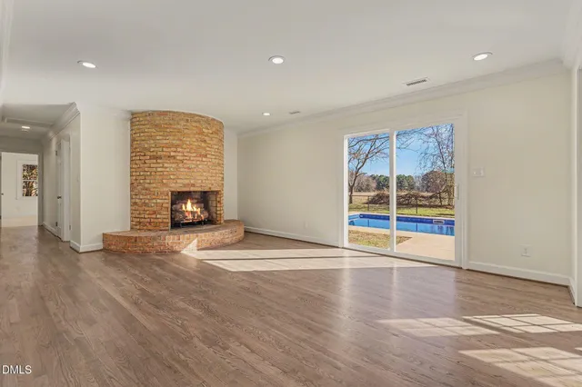 an empty room with wooden floor fire place and windows