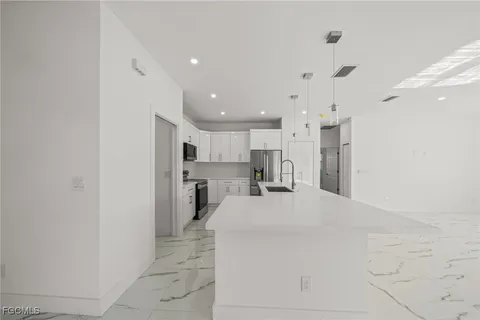 a large white kitchen with kitchen island a stove a refrigerator a sink and a counter top space