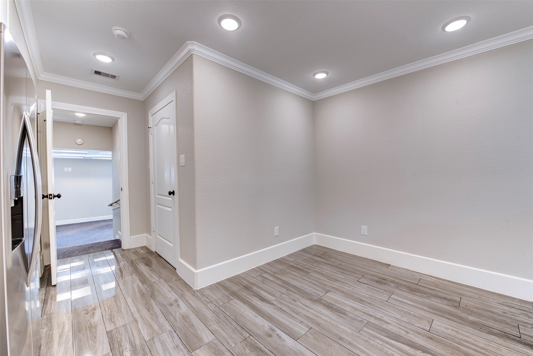 109 Dresden Street Houston, TX 77012 - Photo 21 of 43 This photo showcases a bright, modern room with light wood-style flooring, recessed lighting, and neutral walls. The space is adjacent to a hallway and features a sleek, stainless steel appliance, suggesting proximity to a kitchen or utility area.