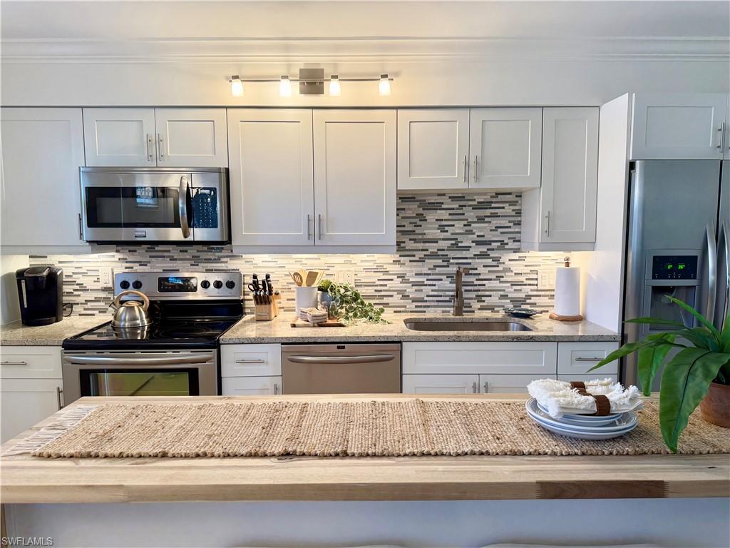 960 7th Street South, Unit 202 Naples, FL 34102 - Photo 8 of 16 a kitchen with kitchen island granite countertop stainless steel appliances a stove refrigerator and microwave