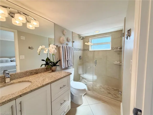 a bathroom with a granite countertop sink a toilet a mirror and shower
