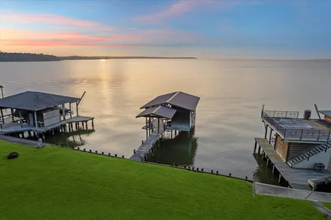 a view of a lake with table and chairs under an umbrella next to a yard