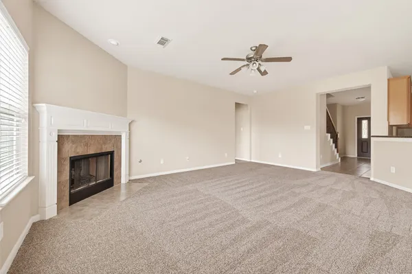 a view of a livingroom with a fireplace a ceiling fan and windows