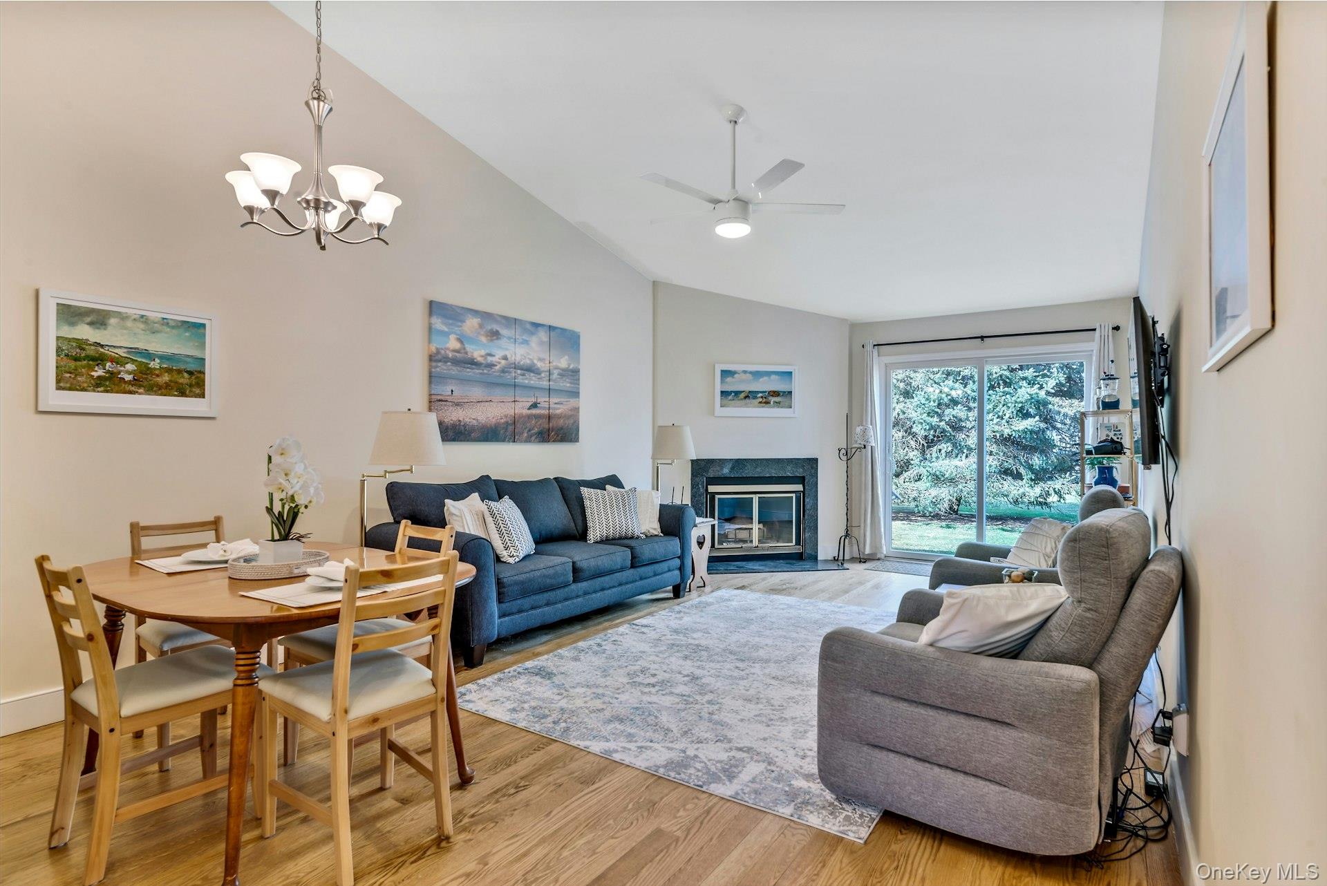 Living area with light wood-type flooring, a high end fireplace, a ceiling fan, a chandelier, and high vaulted ceiling