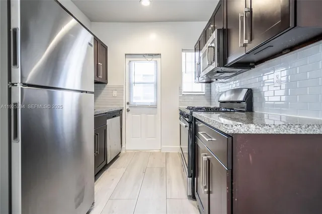 a kitchen with stainless steel appliances granite countertop a refrigerator a stove and a sink with wooden floors