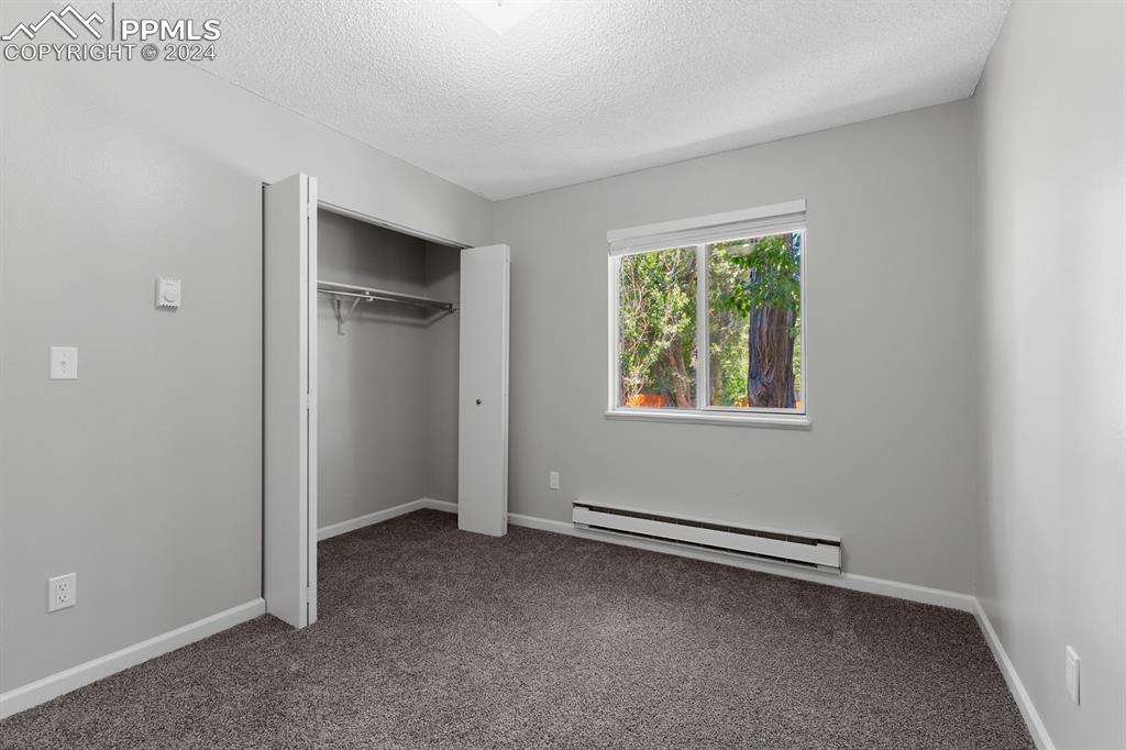 757 Alexander Road, Unit C Colorado Springs, CO 80909 - Photo 13 of 29 Unfurnished bedroom with a baseboard heating unit, dark colored carpet, a closet, and a textured ceiling