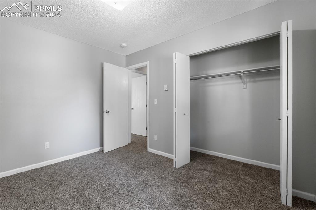 757 Alexander Road, Unit C Colorado Springs, CO 80909 - Photo 14 of 29 Unfurnished bedroom with dark carpet, a closet, and a textured ceiling