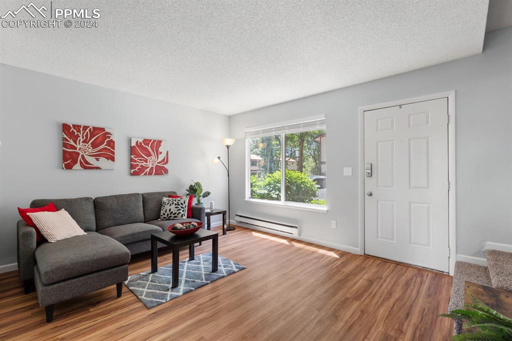 757 Alexander Road, Unit C Colorado Springs, CO 80909 - Photo 7 of 29 Living room featuring hardwood / wood-style floors, a baseboard heating unit, and a textured ceiling