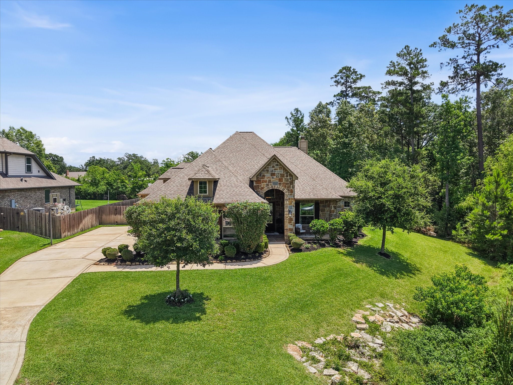 12618 Ranger Court Magnolia, TX 77354 - Photo 41 of 45 Exceptional curb appeal welcomes you home! This gorgeous stone and brick property features an extended driveway, a 3-car garage, and beautifully landscaped front gardens with a vibrant green lawn nestled against a serene backdrop of mature trees.