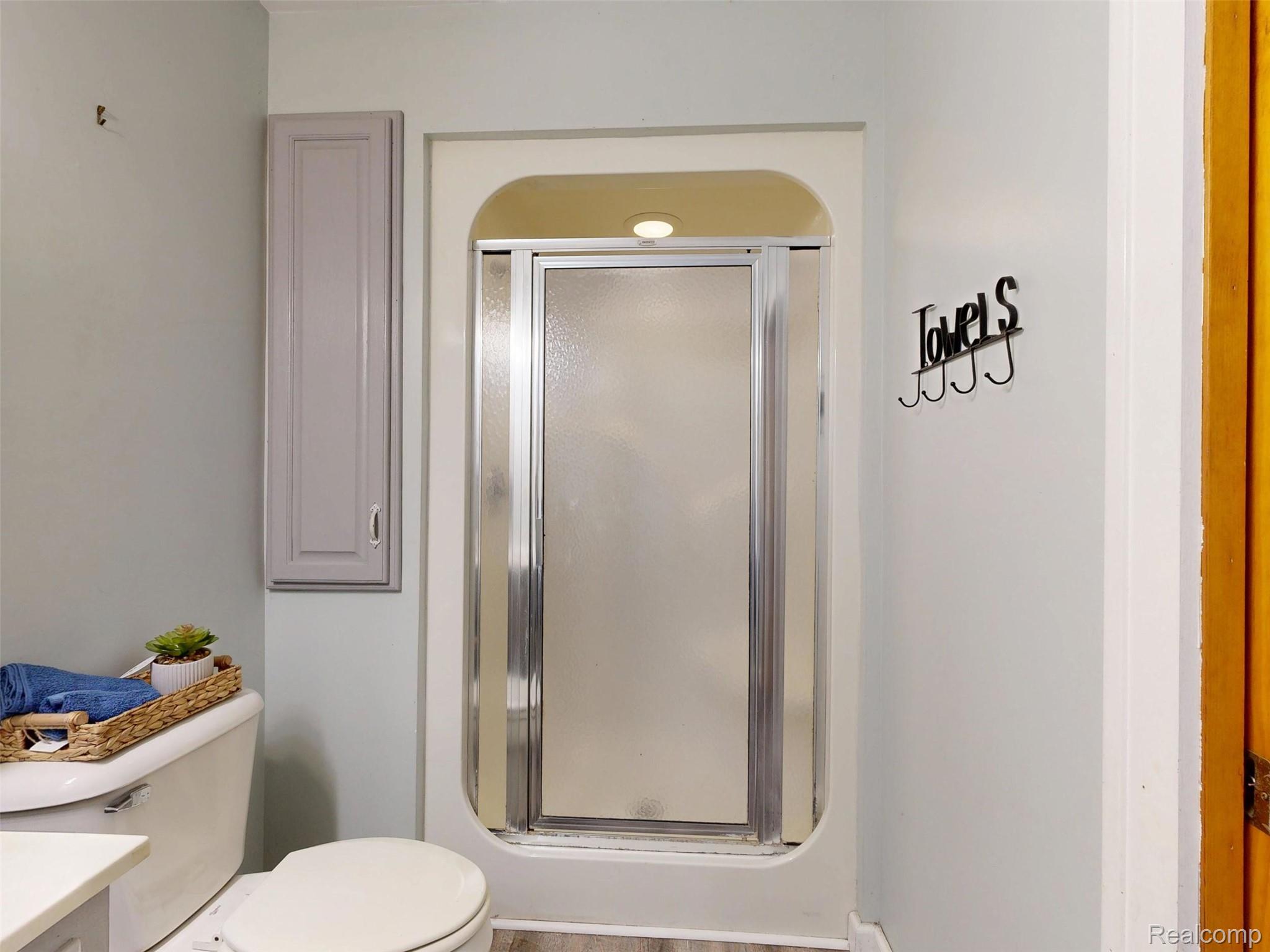 12930 Wilkinson Road Freeland, MI 48623 - Photo 61 of 76 Enclosed shower with sliding glass doors, a wall-mounted storage cabinet, and wood-finish flooring