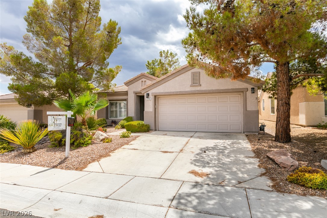 Mature trees frame the concrete driveway leading to a classic stucco facade and garage.