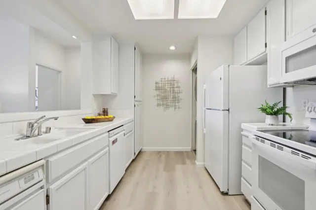 a view of a kitchen with a sink and dishwasher a refrigerator with white cabinets
