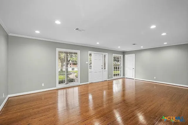 an empty room with wooden floor ceiling fan and windows