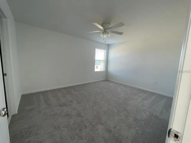 an empty room that has a chandelier fan and a window