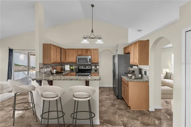 a kitchen with stainless steel appliances kitchen island granite countertop a refrigerator a stove a sink a dining table and chairs with wooden floor