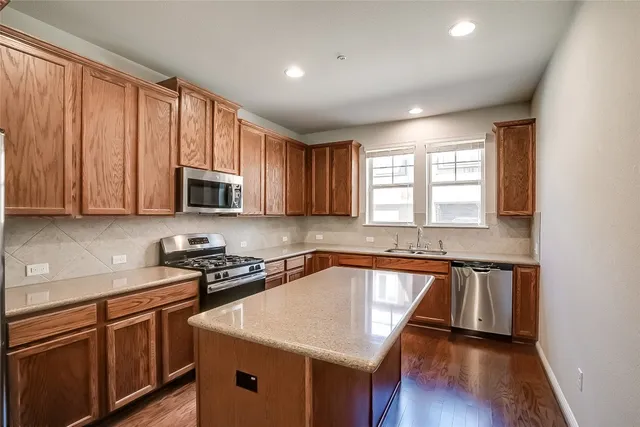 a kitchen with stainless steel appliances granite countertop a stove a refrigerator a sink dishwasher and wooden cabinets with wooden floor