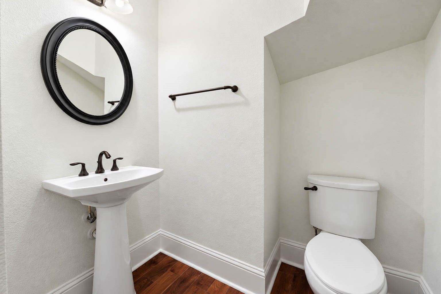 5403 Mesquite Ridge Street Fulshear, TX 77441 - Photo 24 of 42 The downstairs powder bathroom is a convenient spot for guests, with a classic pedestal sink, a round framed mirror, and wood flooring. Generous trim adds a finished touch to this tucked away space.