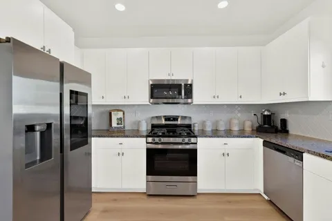 a kitchen with stainless steel appliances granite countertop a stove a refrigerator and a white cabinets