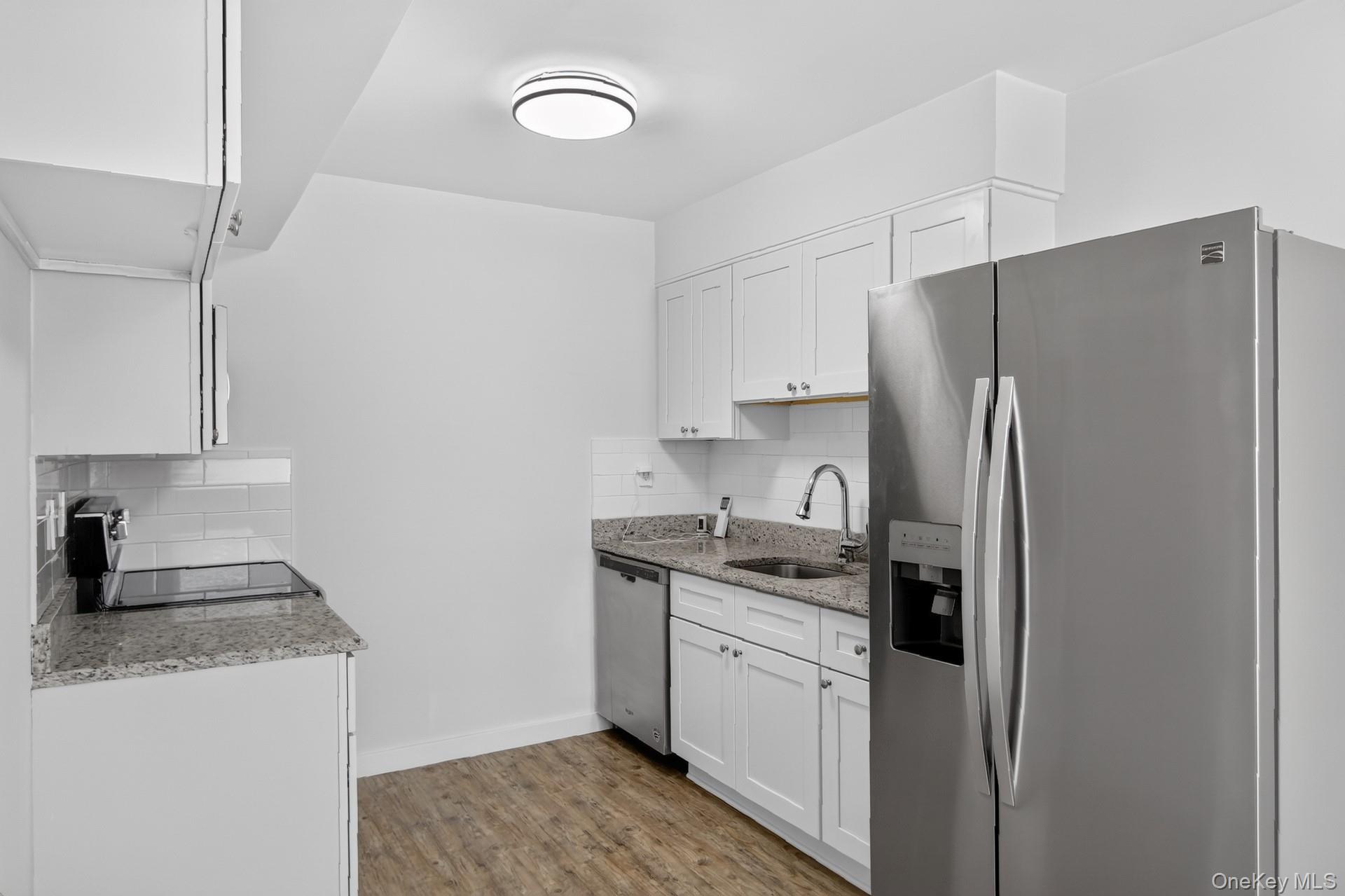26 Cooper Road, Unit 414 Poughkeepsie, NY 12603 - Photo 19 of 24 Contemporary kitchen featuring white cabinetry, granite-finish countertops, subway tile backsplash, stainless steel appliances, and wood-finish flooring