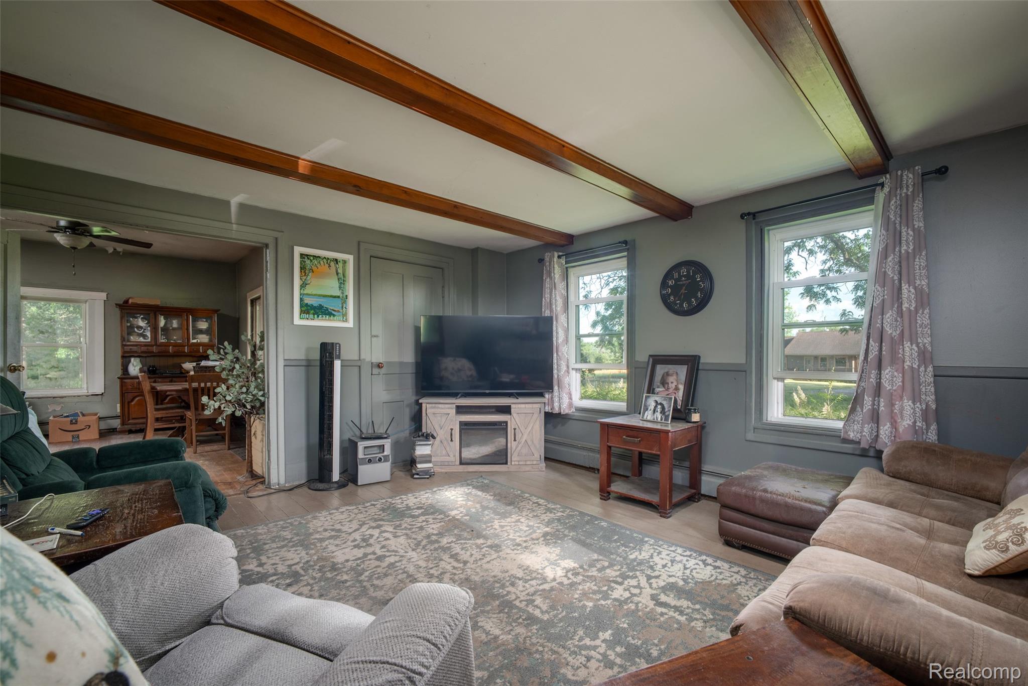 13882 Curtis Road Grass Lake, MI 49240 - Photo 5 of 35 Living area featuring exposed ceiling beams, light wood-finish flooring, and a wall-mounted television console with an integrated electric fireplace