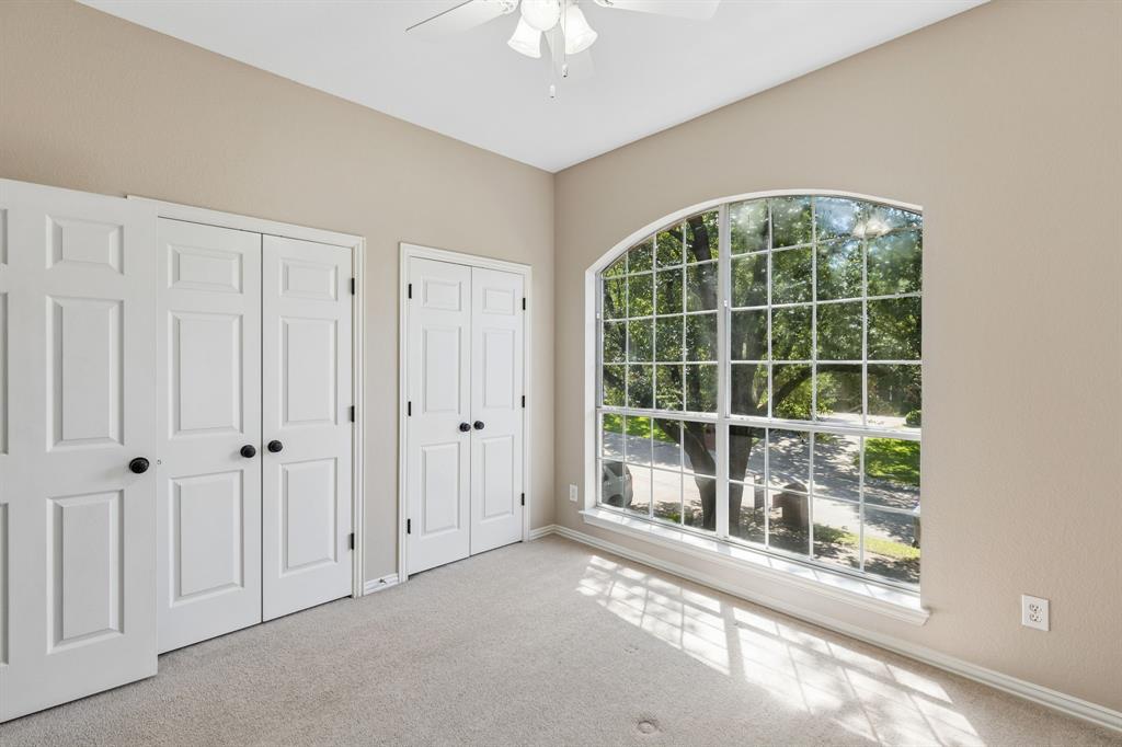 2925 Sunset Ridge McKinney, TX 75072 - Photo 16 of 33 Spacious upstairs secondary bedroom filled with natural light from a dramatic oversized arched window, featuring plush carpeting and generous closet space for a bright and inviting retreat.