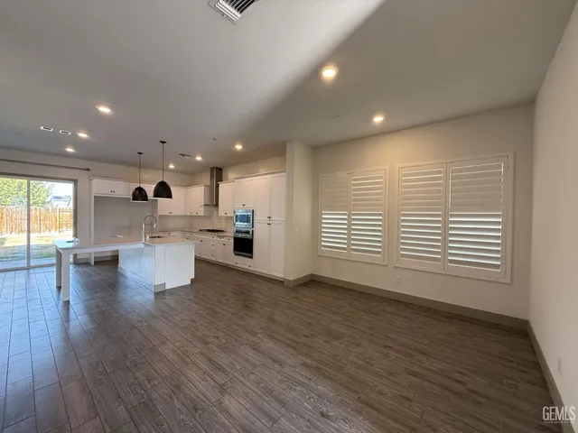 a view of an empty room with wooden floor and a kitchen