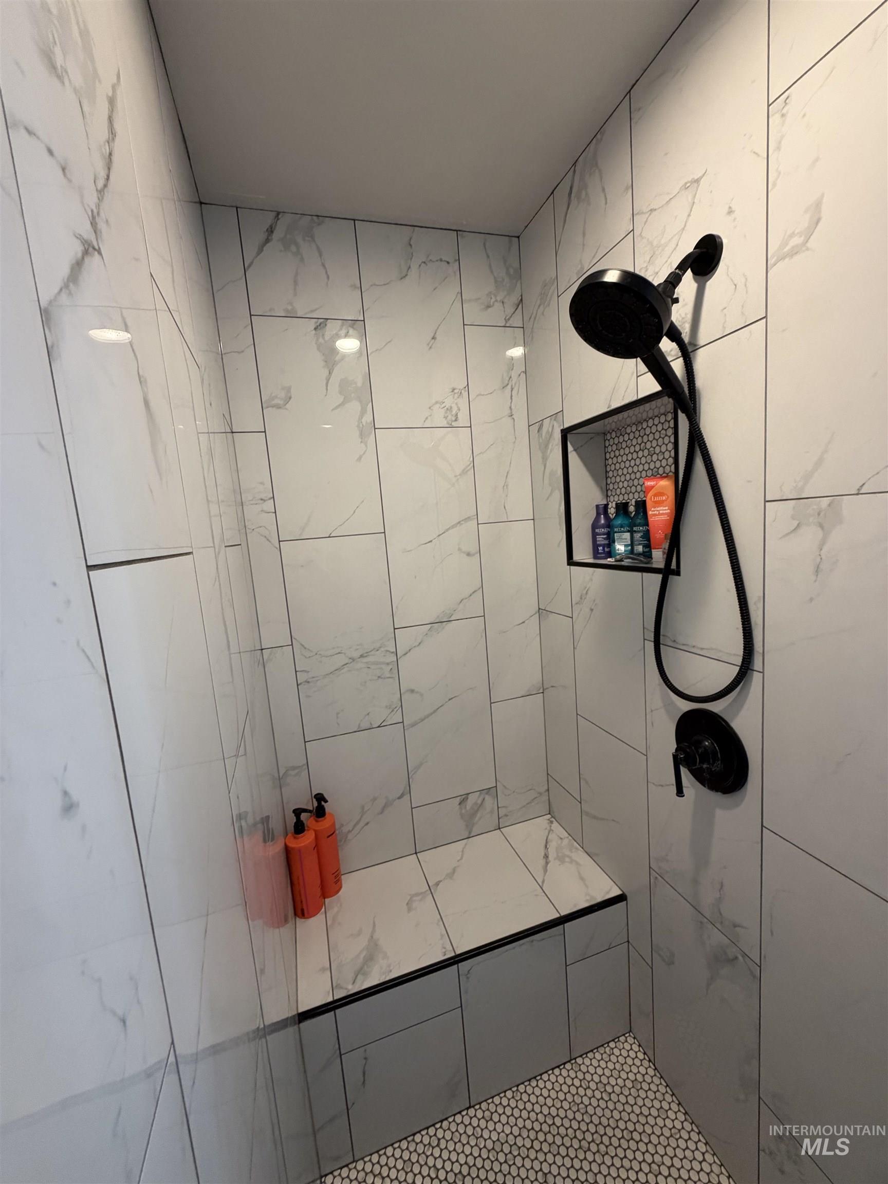 880 Jenkins Creek Road Weiser, ID 83672 - Photo 30 of 43 Walk-in shower featuring large format white and grey marbled tile walls, a built-in bench with a contrasting black trim, and a matte black shower fixture