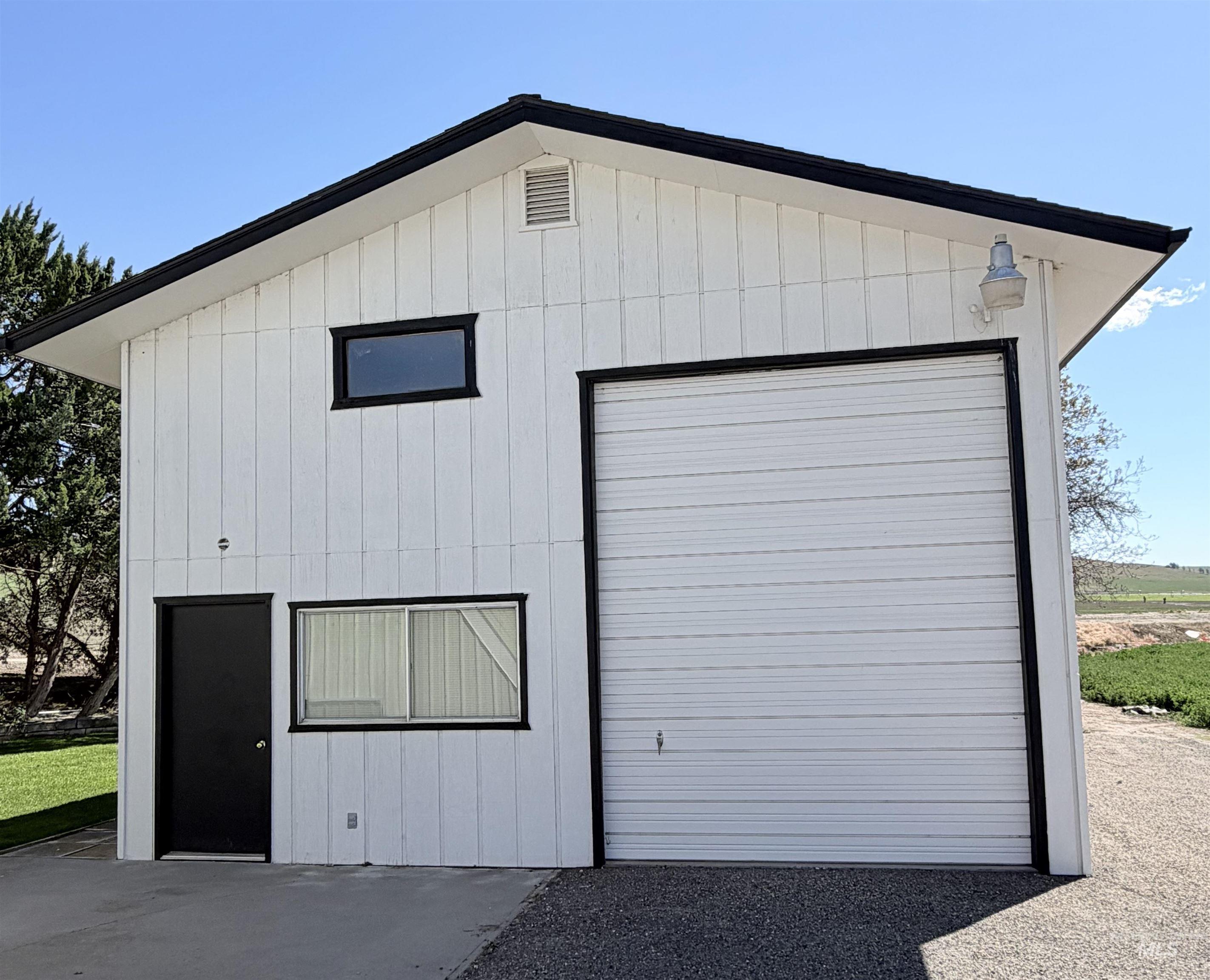 880 Jenkins Creek Road Weiser, ID 83672 - Photo 41 of 43 Two-story white vertical siding structure featuring a large garage door with black trim, a black entry door, and multiple windows
