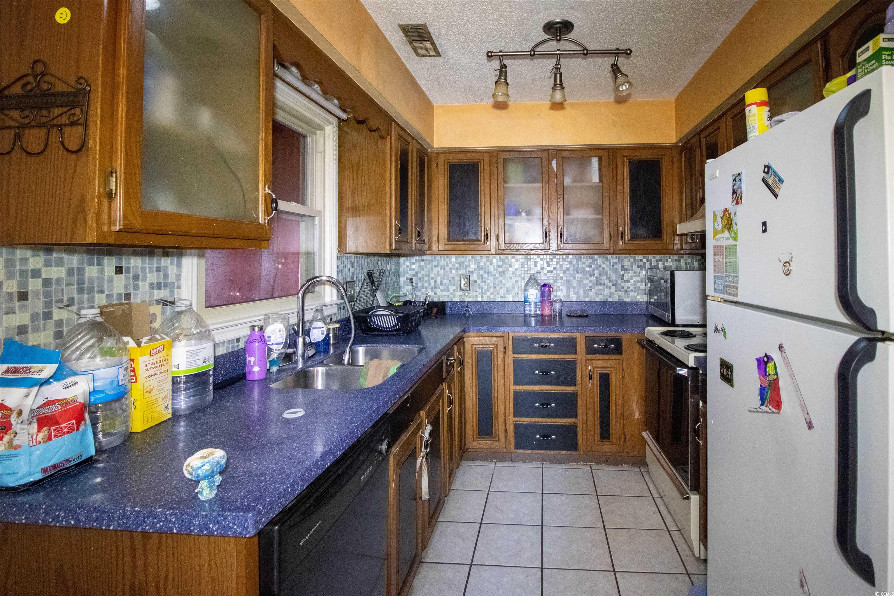 41 Channing Drive Little River, SC 29566 - Photo 4 of 19 Kitchen featuring white appliances, brown cabinetry, light tile patterned floors, and a textured ceiling
