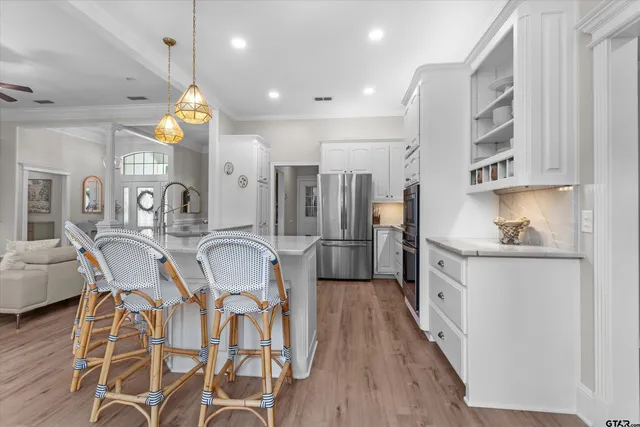 a kitchen with stainless steel appliances granite countertop a refrigerator a sink dishwasher a stove and white cabinets with wooden floor