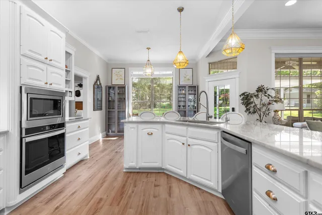 a kitchen with stainless steel appliances granite countertop a stove a sink and white cabinets with wooden floors