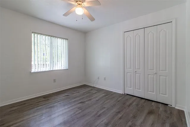 a view of an empty room with wooden floor and a ceiling fan