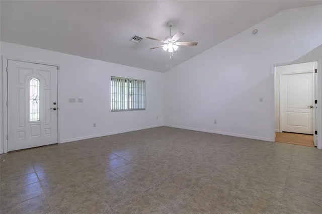 an empty room with chandelier fan and windows