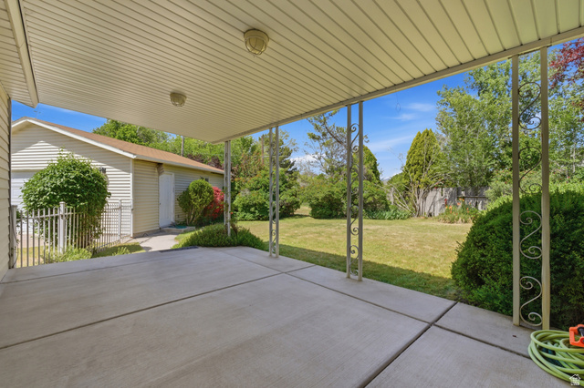 148 Tennyson Avenue Sandy, UT 84070 - Photo 43 of 55 Covered concrete patio with decorative metal support posts, offering views of a spacious lawn and mature landscaping