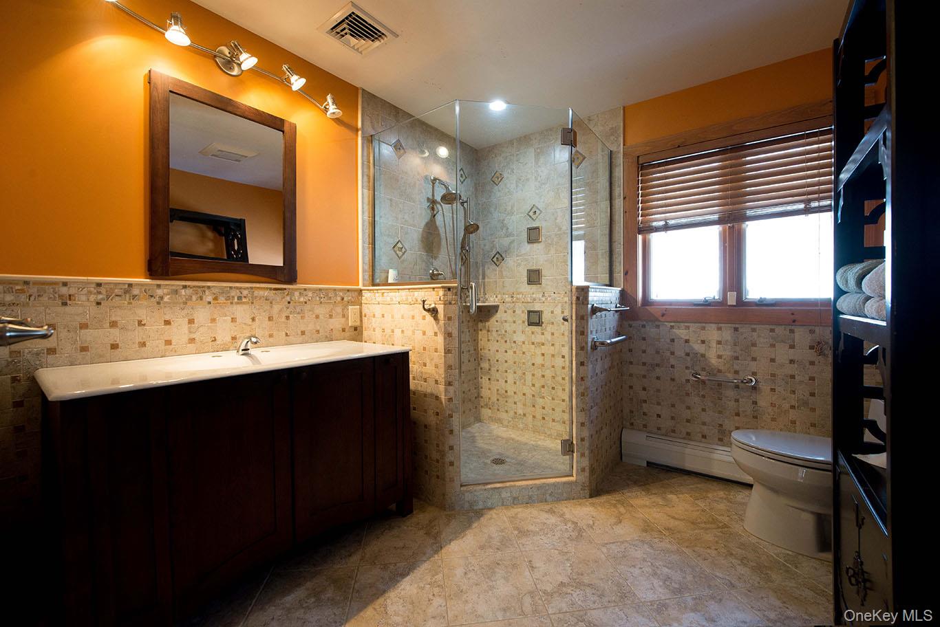 1644 Lakes Road Monroe, NY 10950 - Photo 26 of 50 Full bathroom featuring vanity, tile walls, a stall shower, a baseboard heating unit, and a wainscoted wall