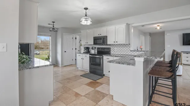 a kitchen with stainless steel appliances granite countertop a stove top oven a sink a refrigerator and white cabinets