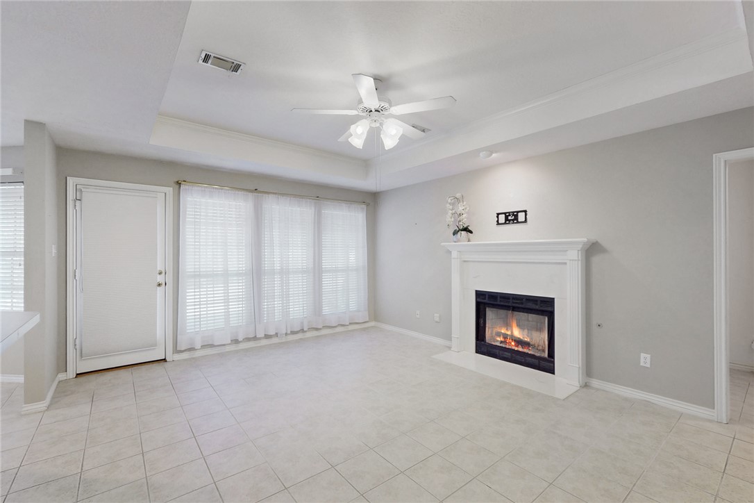 5901 Sheffield Terrace Lane Bryan, TX 77802 - Photo 5 of 31 Unfurnished living room featuring a raised ceiling, a ceiling fan, a fireplace with flush hearth, and light tile patterned flooring