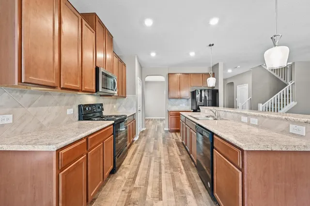 a large kitchen with stainless steel appliances granite countertop plenty wooden cabinets counter space a sink and a wooden floor
