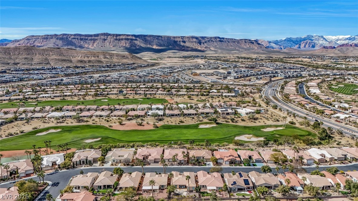 5015 Rivedro Street Las Vegas, NV 89135 - Photo 84 of 91 An aerial panorama showcases a vast residential community nestled alongside a golf course, with distant mountains providing a dramatic backdrop.